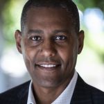 Ermias Kebreab headshot smiling in dark suit with white collared shirt and green muted background